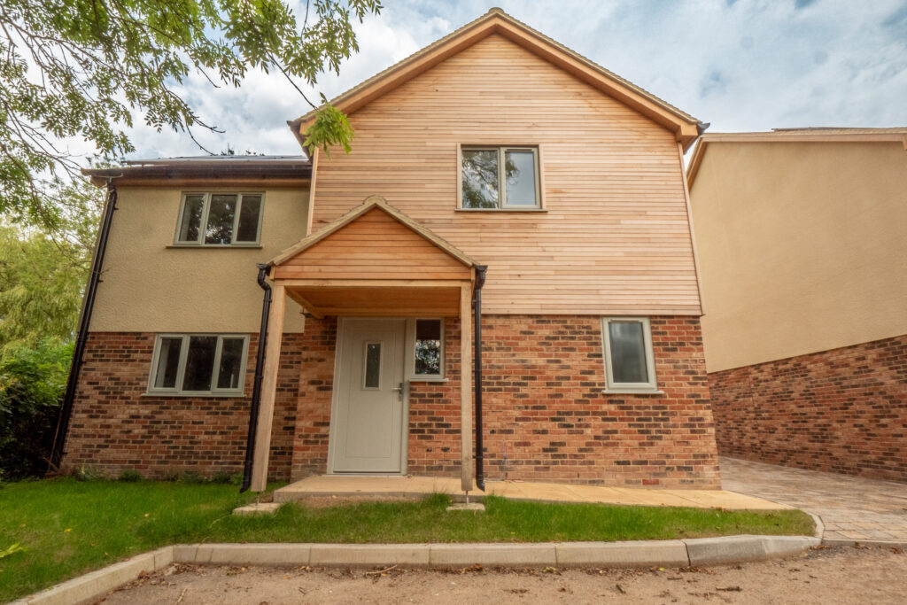 Completed new-build home with timber cladding, brick plinth and paved frontage