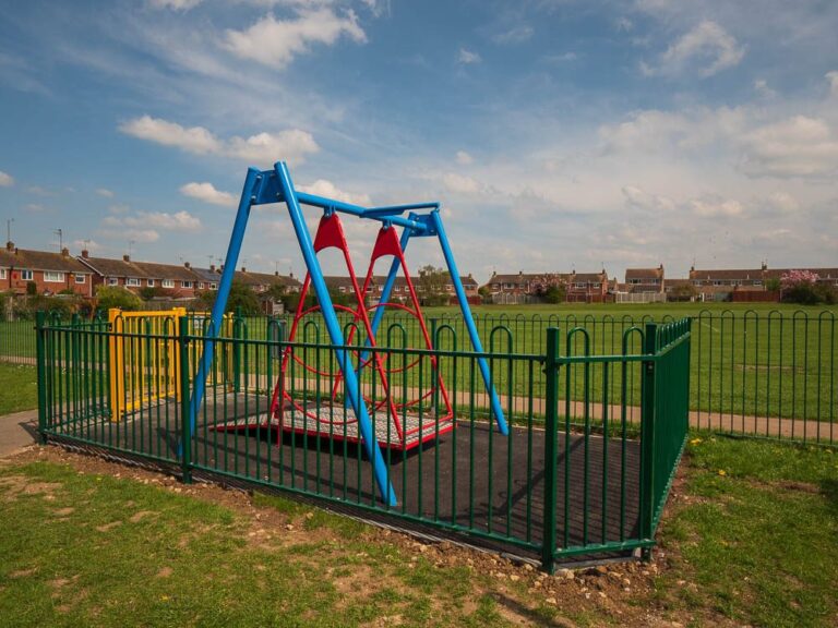 Fenced enclosure around a wheelchair-accessible swing on a playing field.