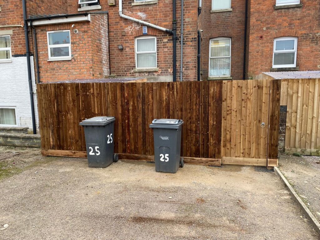 Closeboard fence screening a bin store area.