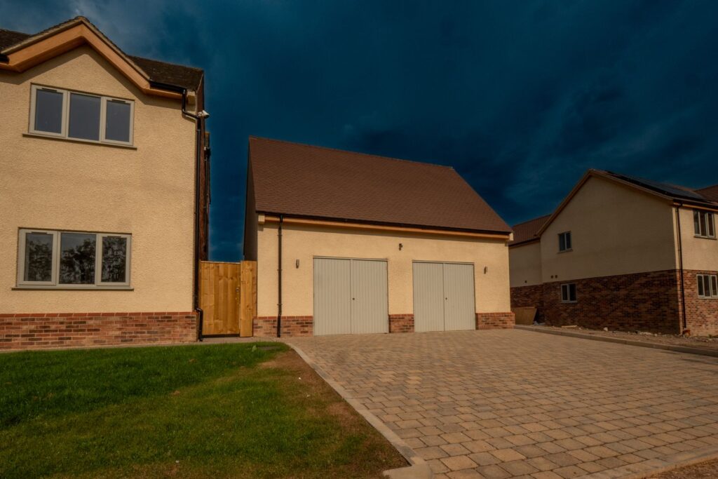 A kerb-edged block-paved driveway curves from the verge to a new Gloucestershire double garage.
