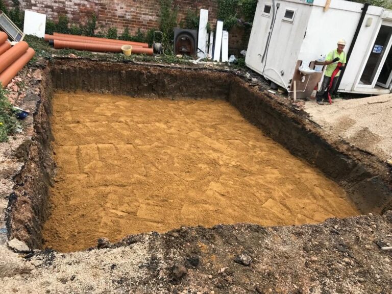 Excavated foundation for a new building beside existing properties.