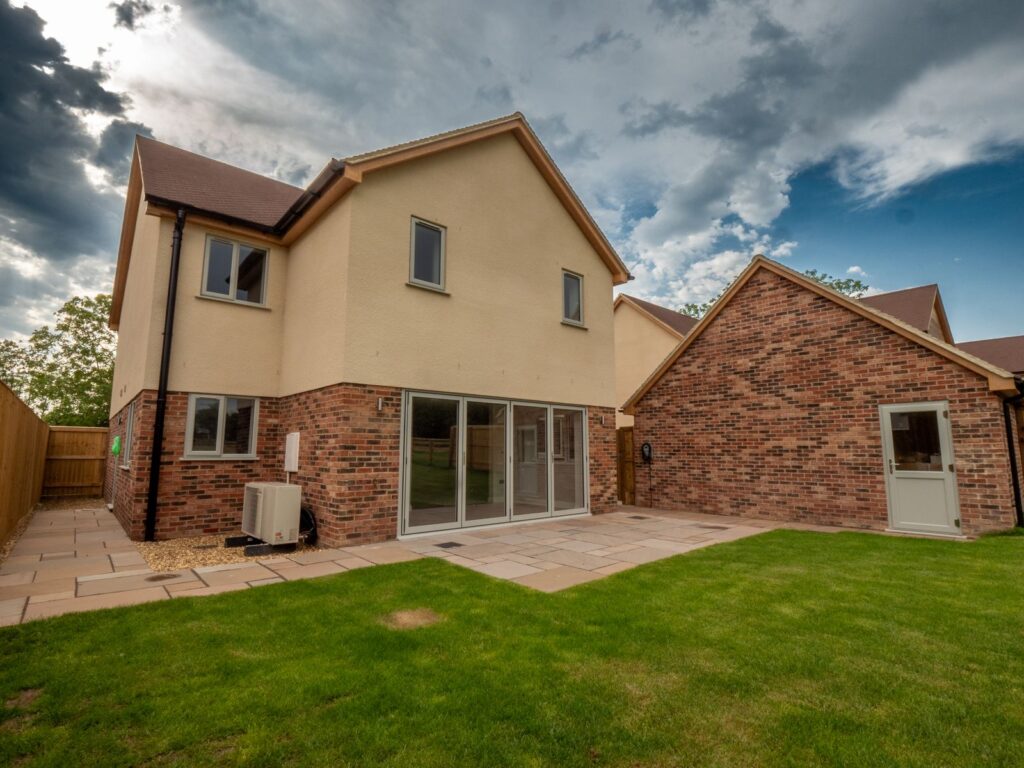 Completed sandstone garden patio paving creates a broad terrace beside this Gloucestershire home and garage.