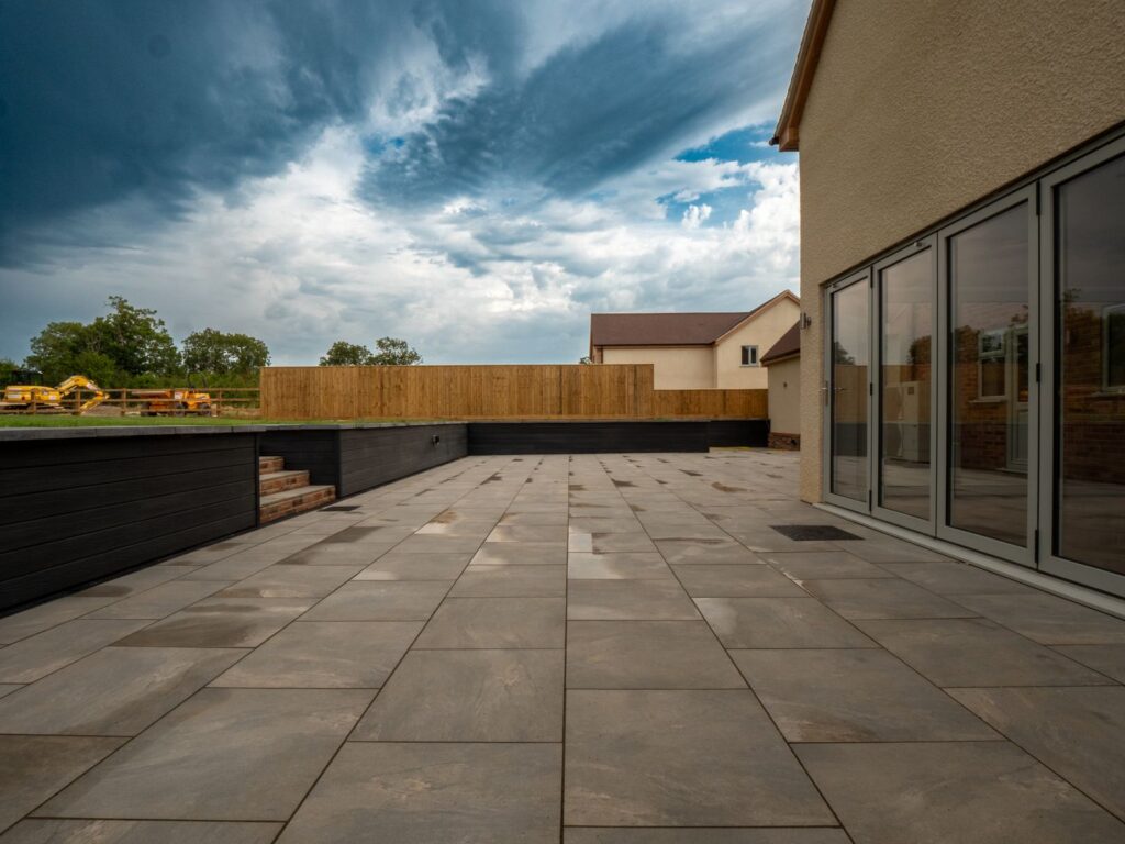 Completed grey porcelain garden patio with raised planters at a Gloucester home.