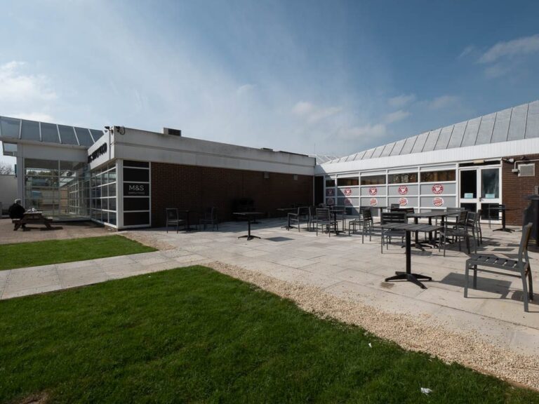 Outdoor seating area with paving and lawn beside the services building at Leigh Delamere.