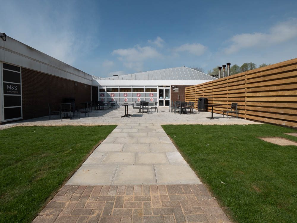 Paved path through lawn to the outdoor seating area at Moto Leigh Delamere Services.