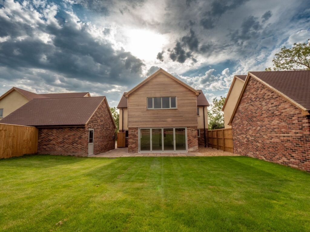 New timber-clad and brick home with completed lawn and paved edge on a Gloucestershire construction project.