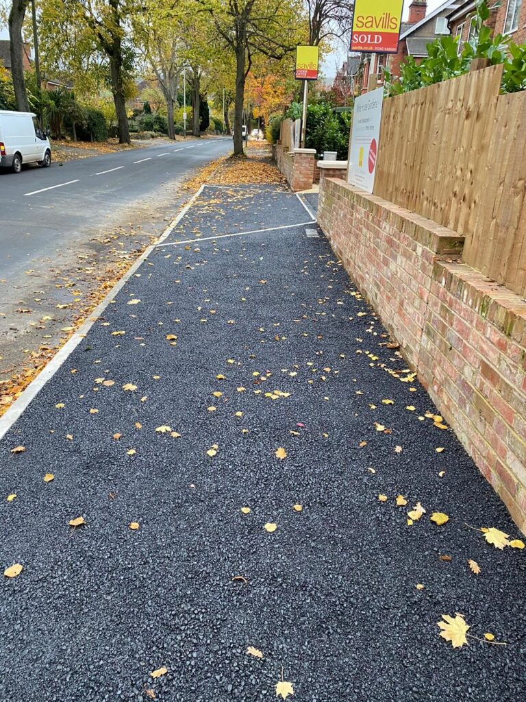 Tarmac footpath with edging beside a brick wall.
