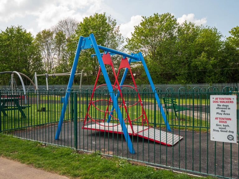 Wheelchair-accessible swing installed in a fenced play area.